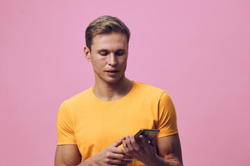 young man using smartphone wearing yellow t-shirt pink background focused on screen digital nomad...
