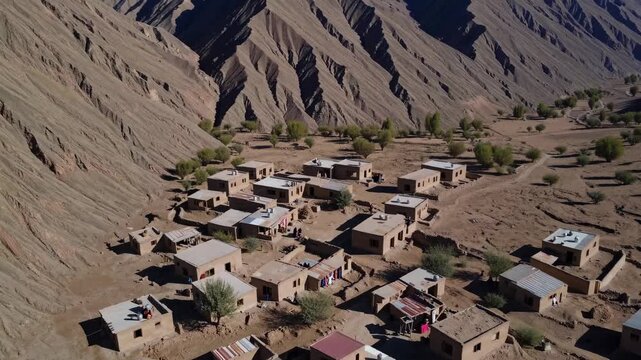 Aerial video view of a remote village nestled in rugged mountains. Captures vast landscapes and dramatic peaks under clear blue skies.