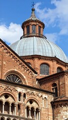 A detailed view of a cathedral dome and intricate facade, showcasing the architectural design and rich terracotta hues against a vibrant blue sky.