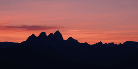 An ethereal blend of orange and red sunlight illuminates the sky, creating a beautiful silhouette of the mountain landscape at dusk