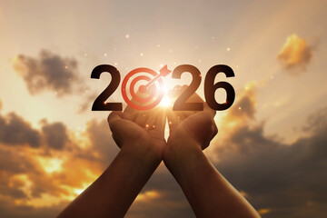 Hands lifting 2026 with a bullseye in the zero, set against a sunrise sky, symbolizing new year...