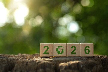 Wooden cubes show 2026 with a green world icon on a natural bokeh background, linking Happy New Year goals with environmental protection and business objectives. sustainability, planning, growth.