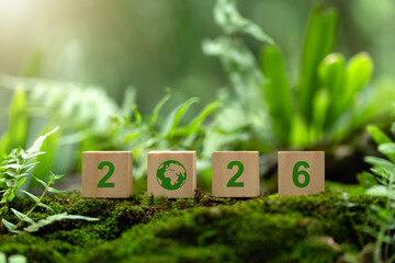 Wooden cubes text 2026 with a green earth icon sit on lush moss, symbolizing New Year goals in environmental protection, sustainability strategy, ESG planning, conservation and responsible growth.