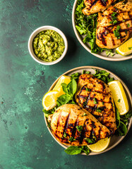 Grilled Chicken Breast with Lemon and Green Sauce on Green Background