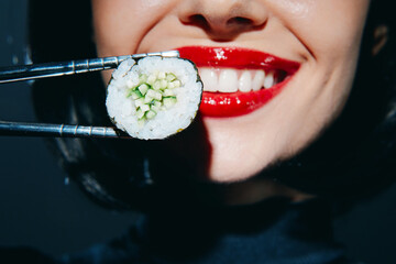 Smiling model holding sushi with chopsticks, vibrant colors and red lips, showcasing culinary...