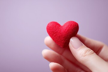 Fototapeta premium A delicate red heart shape held gently in a hand against a soft lavender background.