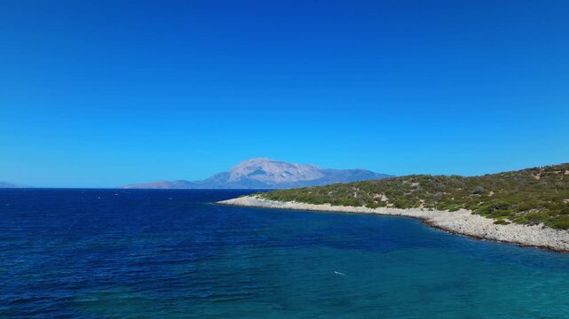Rocky coastline of Samiopoula with lush vegetation and Mount Kerkis rising in the distance, Greece