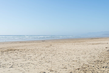 View of pacific ocean from an empty sandy beach with small waves in a distance on a clear calm sunny day in summer. 