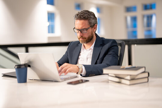 Office workplace. Handsome business man working with laptop at desk in office. Businessman typing on keyboard, online business meeting. Businessman working in office. Office worker using laptop.