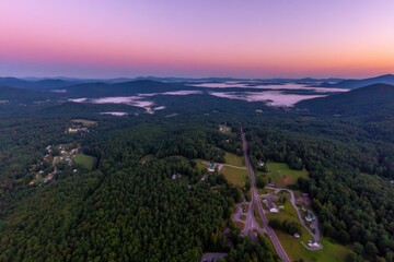 Obraz premium Aerial view of a valley at sunrise, mist clinging to the lower elevations, showcasing a road winding through a landscape of forests, fields, and small settlements