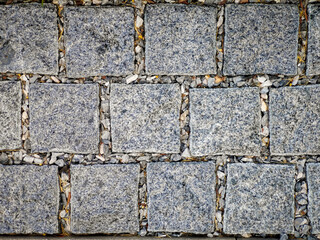 Close-up of square granite tiles with speckled texture and gravel joints. Ideal for abstract backgrounds, architectural surfaces, or outdoor design themes.