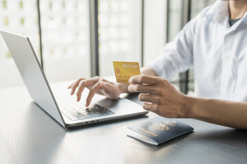 Hand Man Online booking and buying plane tickets using laptop phone and credit card Planning trip travel vacation with passport and ticket