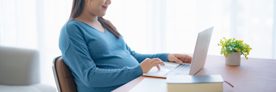 Pregnant asian woman using laptop at home pregnant businesswoman typing on laptop working on remote project in home office pregnancy concept - Powered by Adobe