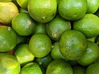 Top-down shot of a pile of fresh limes and a few lemons. The image focuses on the vibrant green and yellow colors and the textured skin of the citrus fruits