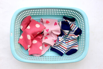 Mixed colorful socks with polka dot, stripe, and heart patterns in a laundry basket.