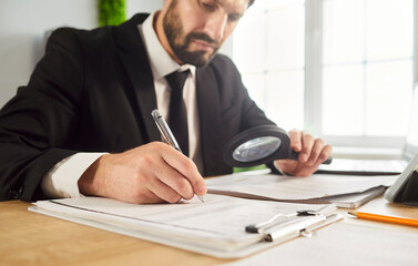 Business audit, scrutiny analysis by businessman reading office documents with magnifying glass in...