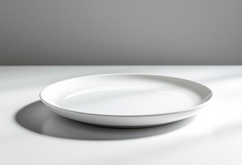 A simple, clean, white plate sits on a white surface, highlighting its smooth texture and minimalist design.