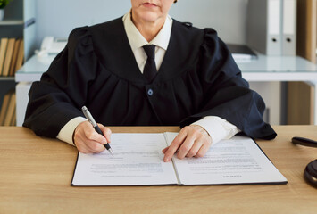 Female judge, wearing robe, writing document, handling legal process, in formal office, dealing...