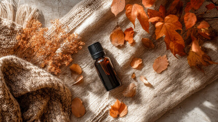 Essential oil bottle lying on cozy sweater with autumn leaves and dry flowers