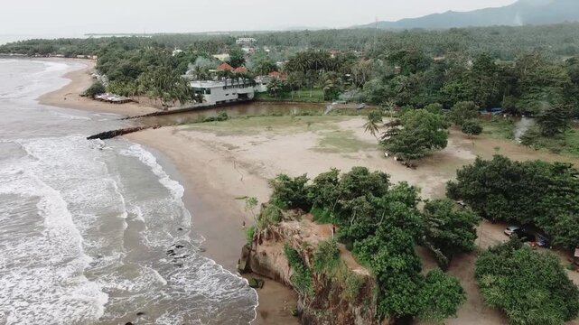 Aerial drone view of Karang Bolong Beach in Anyer, Indonesia, showing the iconic sea cliff, ocean waves, and a lush tropical coastline
