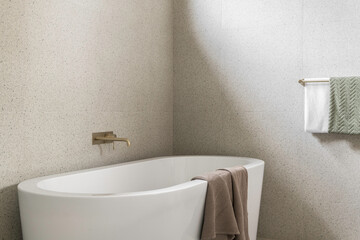 Beautiful natural filled light bathtub in a luxurious modern bathroom. Decorative interior design with hand towels and golden tap. 