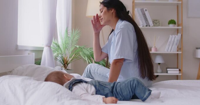 Tired young woman sits beside her peacefully sleeping baby on bed, feels exhaustion and emotional fatigue. Struggles of motherhood, sleepless nights, overwhelming responsibility, mental load concept