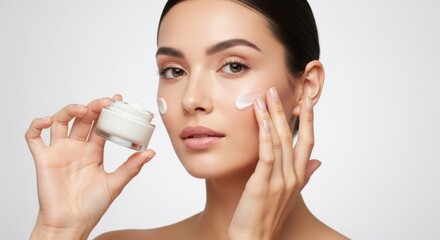 A beautiful woman applies moisturizing cream to her face, holding the jar in her hand
