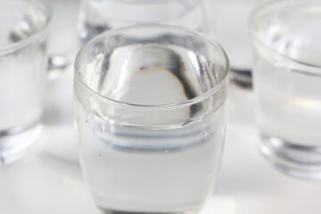 Clear drinking water in various glass cups arranged on a white surface.
