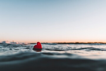 Red heart afloat on calm ocean water at sunset