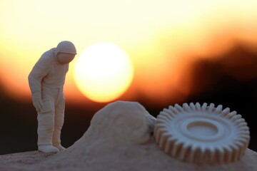Miniature astronaut surveying sunset landscape with damaged equipment