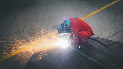 A worker in protective gear welds metal meticulously in a workshop, creating bright sparks that...