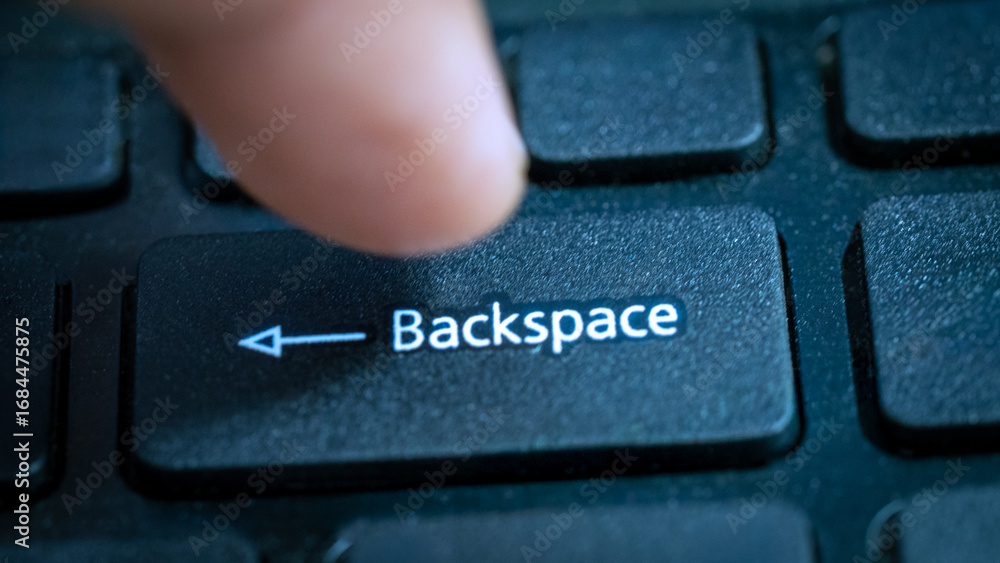 Fototapete a finger is seen pressing the backspace key on a laptop keyboard. the setting suggests a work or stu