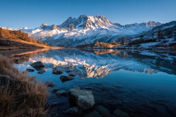 Snow-Capped Mountain Range with Reflection in Alpine Lake, Autumn Foliage, and Rocky Shoreline