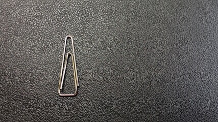 Silver paper clip isolated on a black background, top view. black leather background