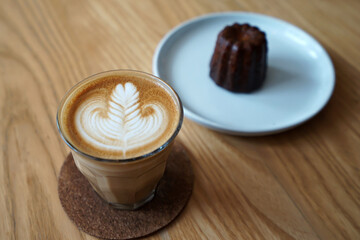 Close up glass of hot latte art coffee served with the Canelé (Canele) de Bordeaux, French bakery pastry confection -rich custardy interior enclosed by a thin caramelized shell