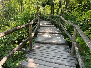 Obraz premium Experience the beauty of Plitvice Lakes with its iconic wooden bridge, surrounded by sparkling blue waters and magnificent waterfalls—a perfect serene escape into nature's embrace.