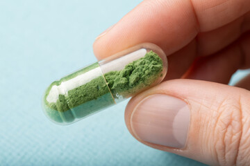 Green herbal capsule with natural supplement powder in hand, alternative medicine concept