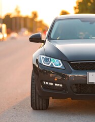 Fototapeta premium A close-up view of a sleek, black car's front end on a paved road, bathed in the warm glow of sunset.
