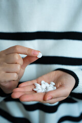 Close-up of woman pouring white pills from bottle into hand, representing medication and...