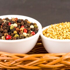 Two small white bowls of mixed peppercorns and mustard seeds rest on a woven basket