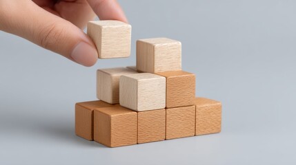 Hand Placing Wooden Block on Top of Stacked Wooden Cubes in Neutral Tones for Creative Play, Learning, and Development in Childhood Activities