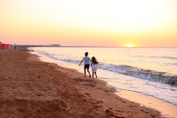 Naklejka premium two children joyfully running along the shoreline at dawn. The soft hues of the early morning sky reflect on the water, creating a magical atmosphere
