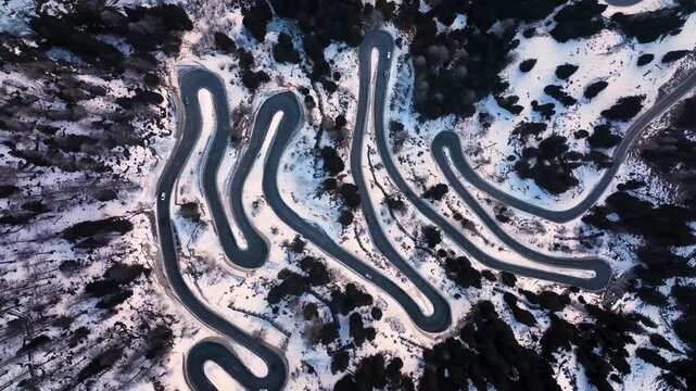 Top-down aerial view of a winding serpentine road ina snowy landscape.