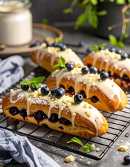 Delicious blueberry pastries, drizzled with white icing and topped with fresh blueberries, sit on a cooling rack.