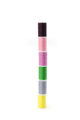 Studio photo of small spools of multicolored sewing threads arranged in a vertical stack, forming a small tower, isolated on a clean white background