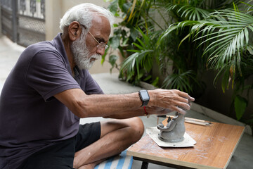 Indian old man crafting an eco-friendly clay Ganesh idol for Ganesh Chaturthi and teaching kids how to do it, sitting outdoors in a garden
