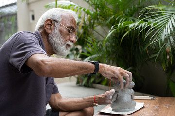 Indian old man crafting an eco-friendly clay Ganesh idol for Ganesh Chaturthi and teaching kids how...