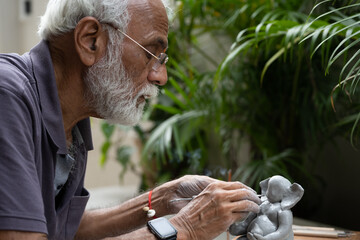 Indian old man crafting an eco-friendly clay Ganesh idol for Ganesh Chaturthi and teaching kids how...