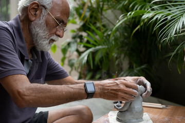 Indian old man crafting an eco-friendly clay Ganesh idol for Ganesh Chaturthi and teaching kids how to do it, sitting outdoors in a garden
