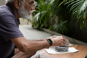 Indian old man crafting an eco-friendly clay Ganesh idol for Ganesh Chaturthi and teaching kids how to do it, sitting outdoors in a garden
